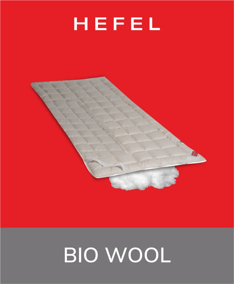 Hefel Bio-Wool mattress pad in a natural cream color, laid out on a bed